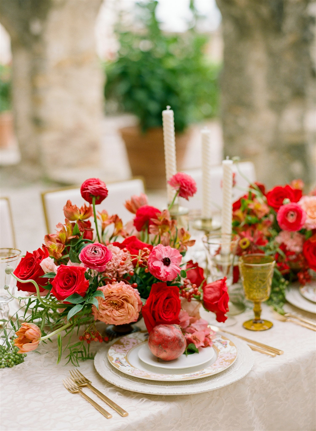 wedding reception table with red floral centerpiece and gold and white place settings