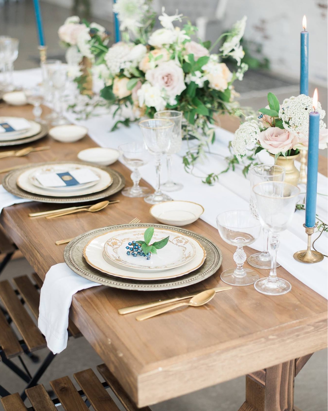 wooden table with gold and white table settings and white floral centerpiece