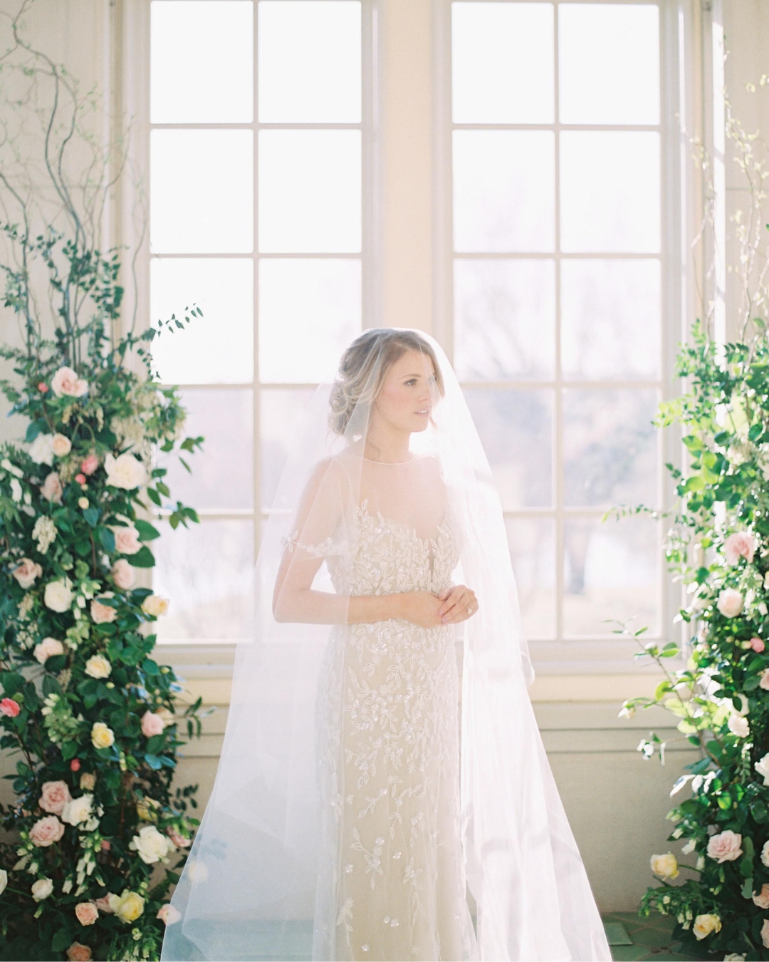 bride draped in her veil standing in front of large windows